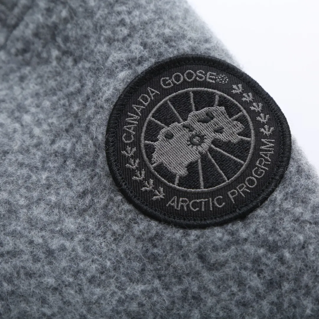 P760 Canada Goose Fleece Badge Button Jacket Fabric selection: Wool blend fabric: The main fabric of this jacket is light gray wool blend fabric to improve the fabric's wear resistance, wrinkle resistance and warmth. Wool provides good warmth and a natural feel, while blended fibers enhance the fabric's practicality and durability.  RIBBED KNIT: The collar, cuffs and hem are ribbed knitted for added stretch and fit.  Production process: The cutting process needs to ensure that the texture and color of the fabric are evenly distributed, especially for this light gray tone, to avoid color differences. The stretchability of wool-blend fabrics needs to be taken into consideration when cutting pieces to ensure dimensional stability of the finished garment.      • Use a sewing needle and thread suitable for wool-blend fabrics to avoid damage to the fabric during sewing. The sewing stitches are even and firm to prevent thread stripping.      • The temperature needs to be controlled during ironing to avoid high temperature damage to the fabric while keeping the fabric smooth and crisp.  Main body splicing: • The front and back body parts, sleeves and other main parts are spliced ​​with flat seams to ensure a smooth silhouette. •Align the fabric texture at the splicing points to keep the appearance neat.     Details such as pockets and cuffs are designed with inset pockets to increase practicality and aesthetics.     The splicing areas are reinforced to improve durability.  Armband: The white round armband on the left arm is an important part of the brand identity and is finely sewn to ensure it is strong and flat.  Dark gray and light gray Size: S M L XL